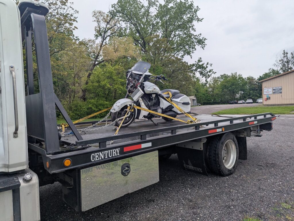 A white motorcycle being transported on a flatbed tow truck by First Hand Towing & Recovery in Fort Wayne, IN.