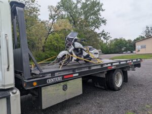 A white motorcycle being transported on a flatbed tow truck by First Hand Towing & Recovery in Fort Wayne, IN.