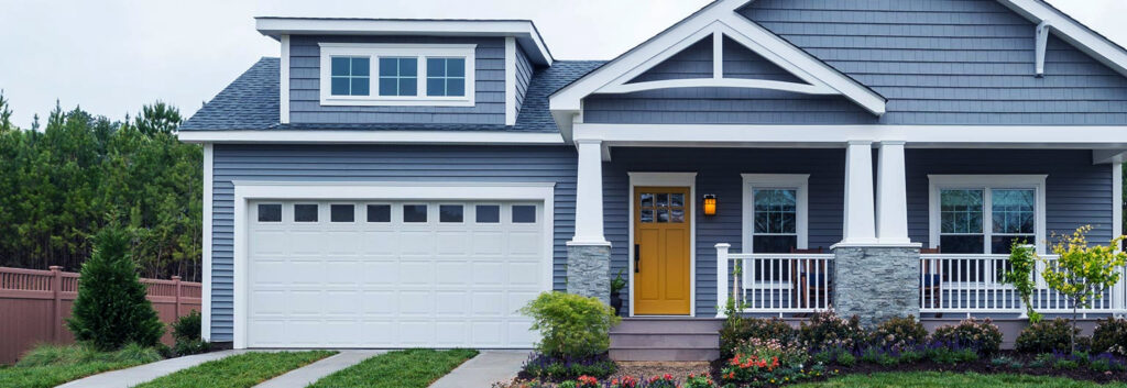 A white panel garage door with windows on a blue residential house, installed by K & B Door Co. in Las Vegas, NV