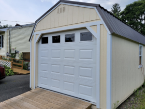 A white panel garage door with top windows installed on a light yellow shed by Champion Overhead Door in Brattleboro, VT.