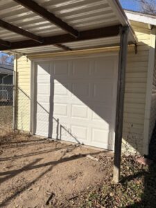 A newly installed white panel garage door on a yellow shed or detached garage by The Door Pros in Wichita, KS