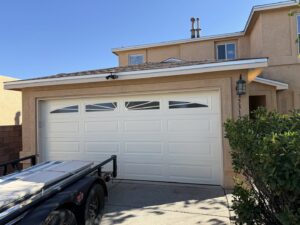 A newly installed white panel garage door with decorative windows on a residential home by Quality-Brand Garage Doors in Rio Rancho, NM.