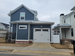 A white paneled garage door with decorative windows on a blue house, installed by Garage Door Sales & Repair in Conway, AR.