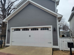 A newly installed white paneled garage door with decorative windows on a grey house by Garage Door Sales & Repair in Conway, AR.
