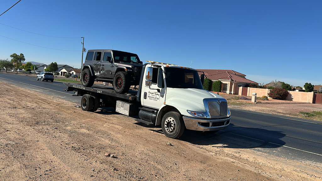 A white passenger van being transported on a flatbed tow truck by Crisanto Towing in Phoenix, AZ.