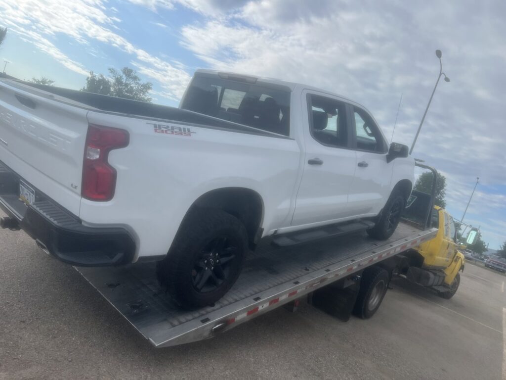 A white pickup truck loaded onto a yellow flatbed tow truck by Geely Towing in Fargo, ND.