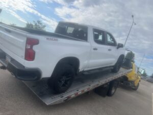 A white pickup truck loaded onto a yellow flatbed tow truck by Geely Towing in Fargo, ND.