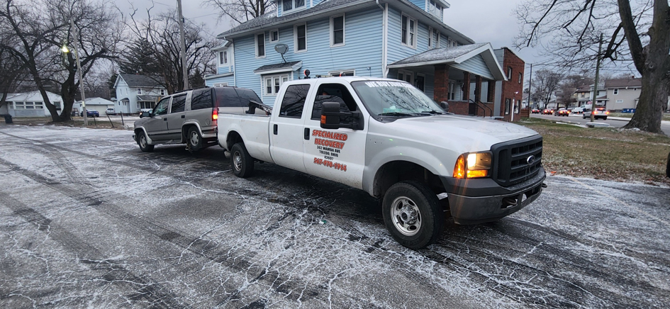 A white pickup truck from Boyz Automotive & Towing towing a grey SUV with a tow bar in Toledo, OH.