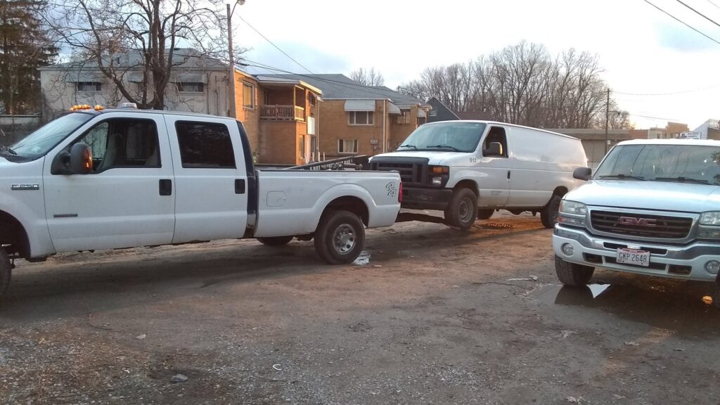 A white pickup truck from Boyz Automotive & Towing towing a white van with a tow bar in Toledo, OH.