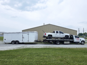 Montes Towing Services flatbed truck towing a white pickup truck and a large enclosed trailer in Indianapolis, IN.