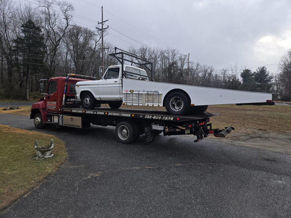 A white pickup truck with an extended bed being towed on a flatbed truck by Riggleman Towing in Moorefield, WV.