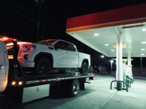 A white pickup truck being towed at a gas station at night by Tow-Ro Towing in El Paso, TX.