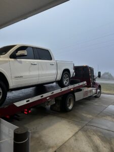 A white pickup truck being transported on a flatbed tow truck from Rick's Towing and Recovery in Lafayette, LA.