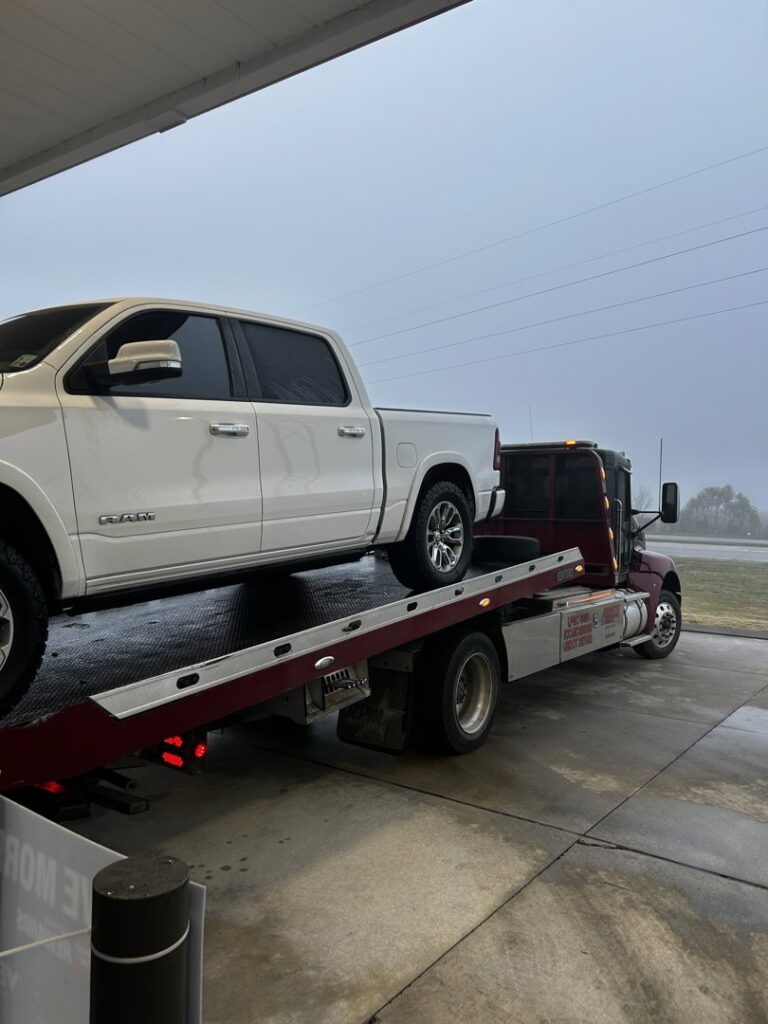 A white pickup truck being transported on a flatbed tow truck from Rick's Towing and Recovery in Lafayette, LA.