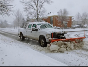 A white pickup truck with an orange snow plow clearing a residential street for Denver Snow Removal in Denver, CO.