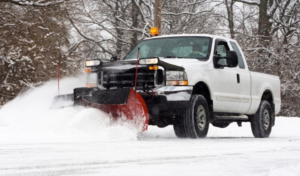 A white pickup truck with a red snow plow clearing snow from a road for Snow Removal St. Louis in St. Louis, MO.