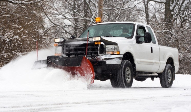 A white pickup truck with a red snow plow clearing snow from a road for Snow Removal St. Louis in St. Louis, MO.
