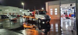 A white pickup truck being towed on a flatbed tow truck at night by Ibanez Towing Service LLC in San Jose, CA.