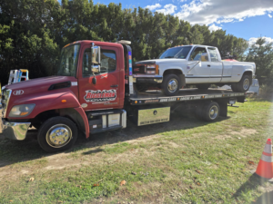 A white pickup truck being transported on a flatbed tow truck by Riggleman Towing in Moorefield, WV.