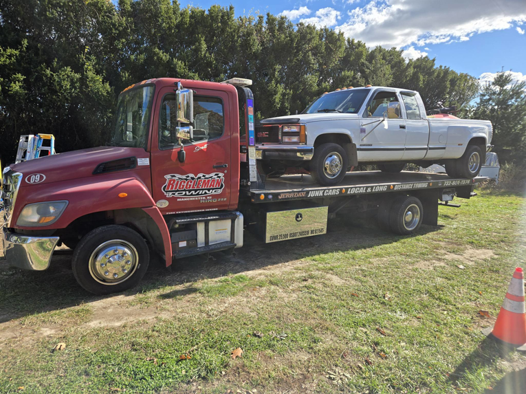 A white pickup truck being transported on a flatbed tow truck by Riggleman Towing in Moorefield, WV.