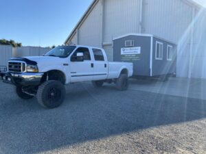 A white pickup truck from Anthony's Towing & Transportation towing a portable construction office in Yuba City, CA.
