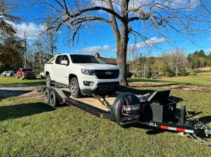 A white pickup truck towing a white SUV on a flatbed trailer from B'ham Trailer Rentals in Alabaster, AL.