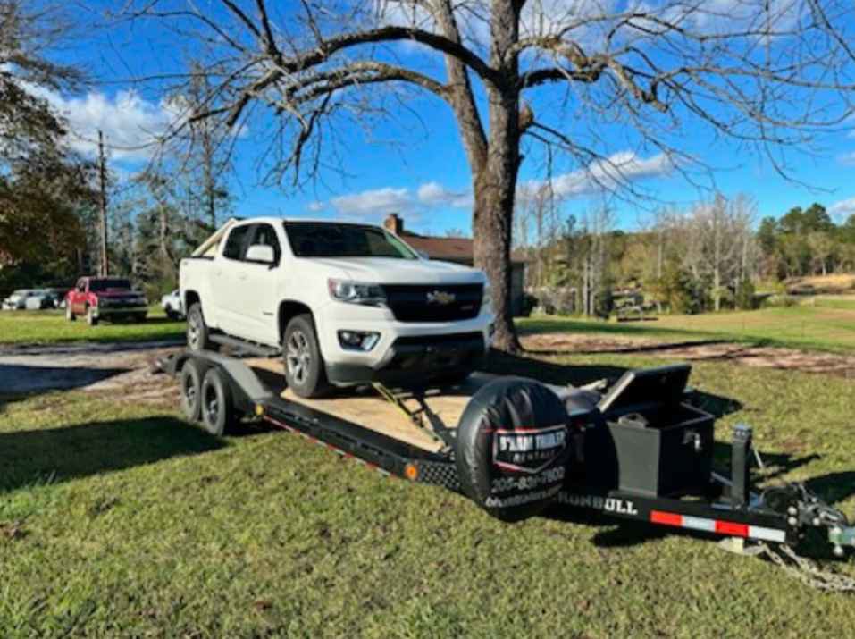 A white pickup truck towing a white SUV on a flatbed trailer from B'ham Trailer Rentals in Alabaster, AL.