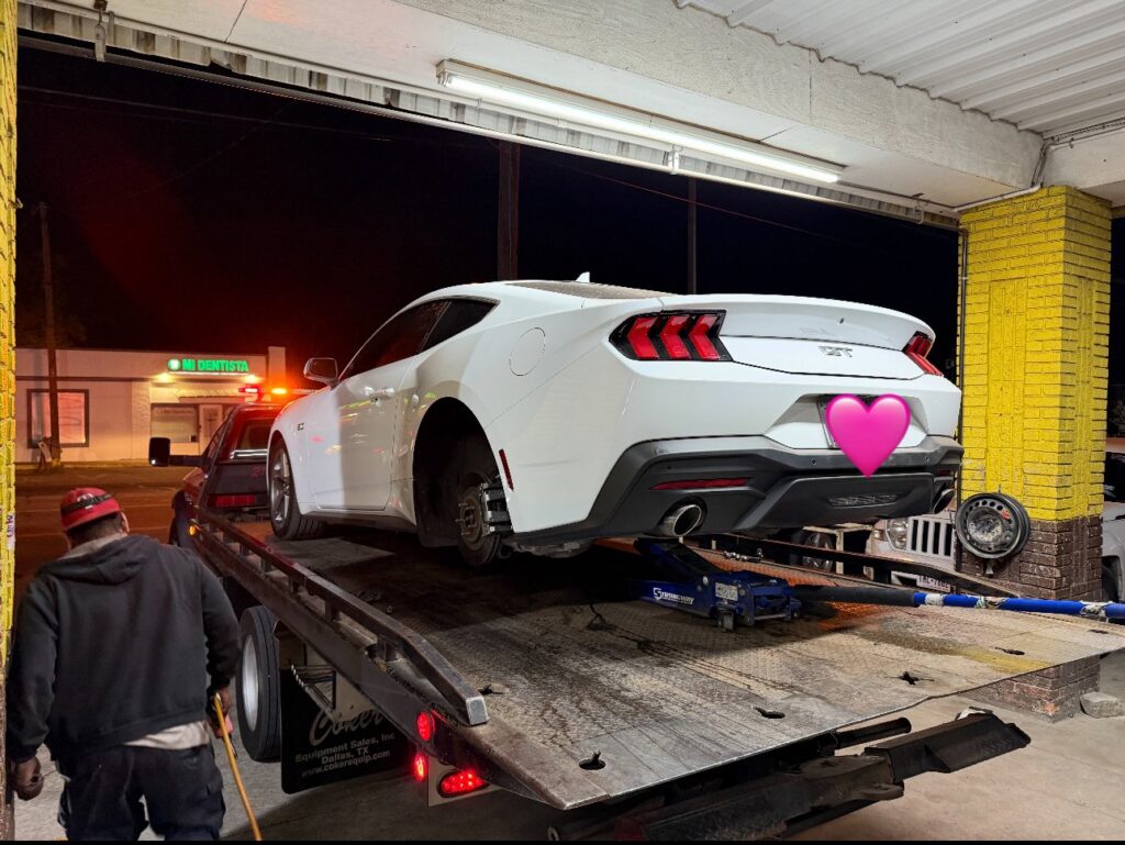 A white pickup truck towing a white car on a trailer for RDZ Towing Service 24/7 in Dallas, TX.