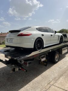 A white Porsche Panamera being transported on a flatbed tow truck by Jay Towing Services in Houston, TX.