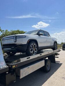 A white Rivian electric pickup truck loaded onto a flatbed tow truck from Jay Towing Services in Houston, TX.