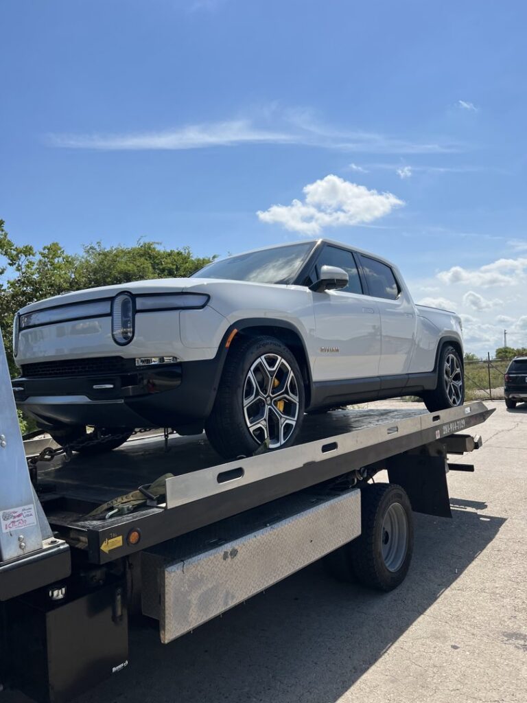 A white Rivian electric pickup truck loaded onto a flatbed tow truck from Jay Towing Services in Houston, TX.