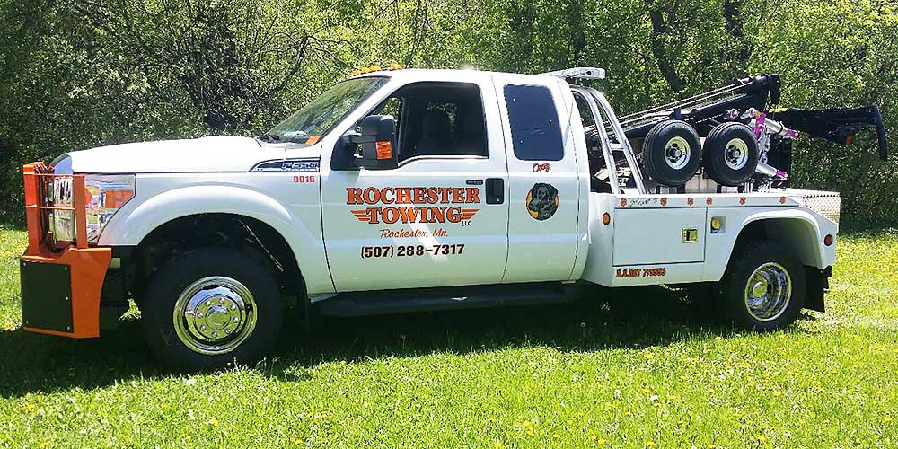 A white Rochester Towing truck with an orange bumper parked on green grass in Rochester, MN.