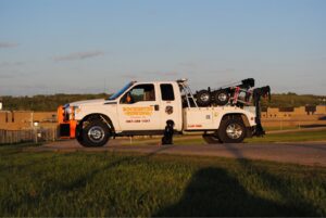 A white Rochester Towing truck with a black dog sitting beside it, parked on a road in Rochester, MN.