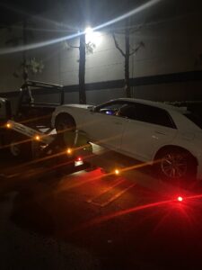 A white sedan being loaded onto a flatbed tow truck by Leos Towing Service at night in Anaheim, CA.