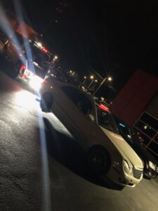 A white sedan being towed by a J & G Towing, LLC truck at night in Greensboro, NC.