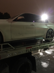 A white sedan loaded onto a flatbed tow truck at night by FSC INC in Omaha, NE.