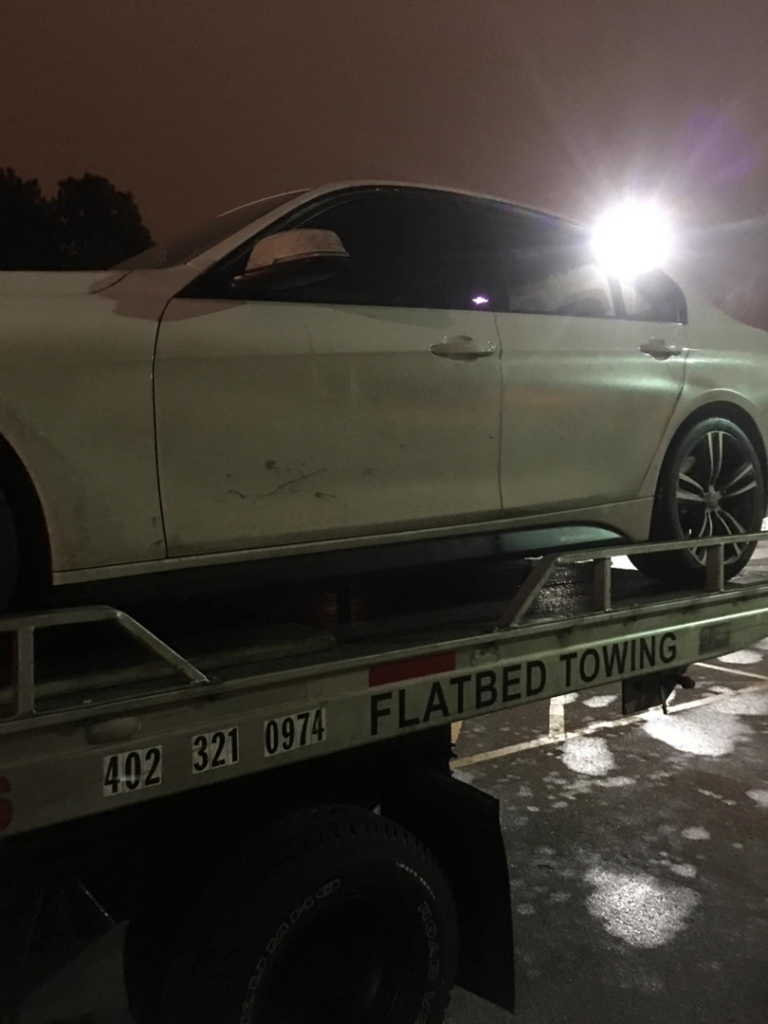 A white sedan loaded onto a flatbed tow truck at night by FSC INC in Omaha, NE.