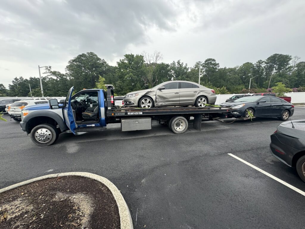 A white sedan being transported on a flatbed tow truck by Hampton Roads Towing Services in Chesapeake, VA.