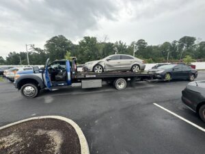 A white sedan being transported on a flatbed tow truck by Hampton Roads Towing Services in Chesapeake, VA.
