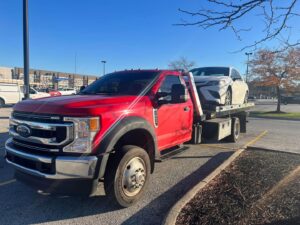 A white sedan being transported on a flatbed tow truck in a parking lot by Quiñones Towing in Cleveland, OH.