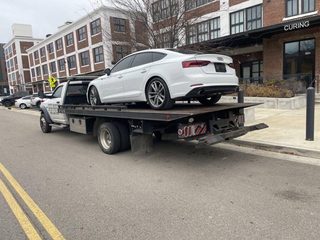 A white sedan loaded onto a flatbed tow truck, providing towing services by Swift Response Road Services, LLC in Memphis, TN.