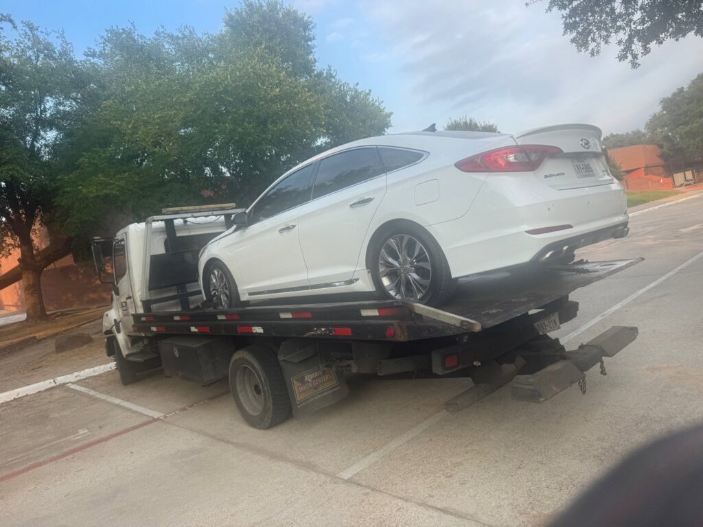 A white sedan being towed on a flatbed tow truck by Black Rhino Towing in Denver, CO.