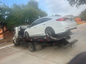 A white sedan being towed on a flatbed tow truck by Black Rhino Towing in Denver, CO.