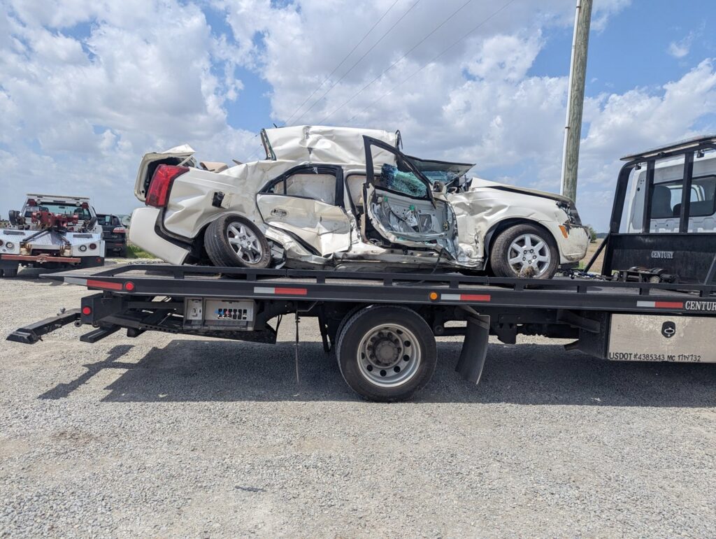 A white severely damaged car being recovered and transported on a flatbed tow truck by First Hand Towing & Recovery in Fort Wayne, IN.
