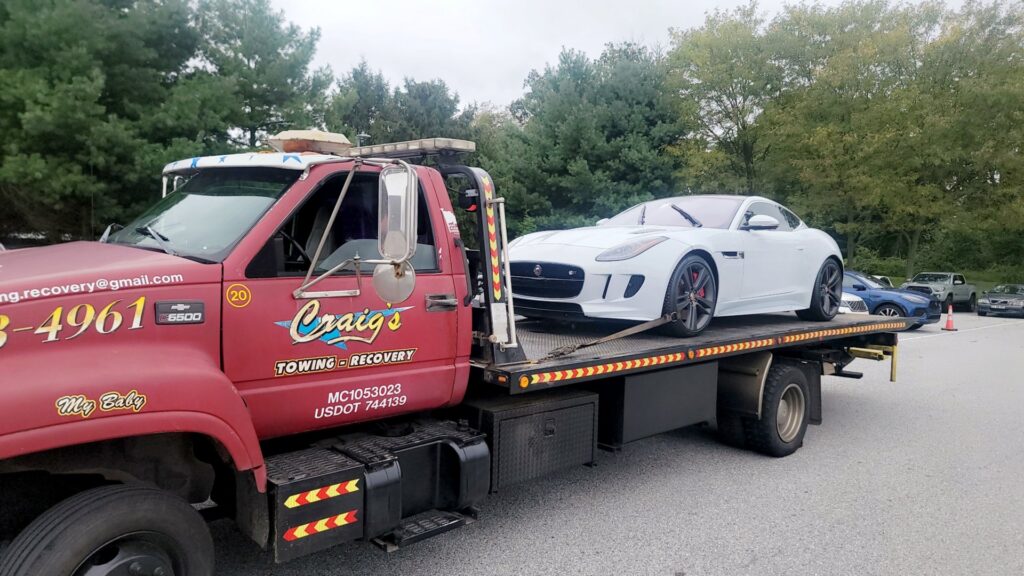 A white sports car being transported on a flatbed tow truck by Craig's Towing & Recovery in New Castle, DE.