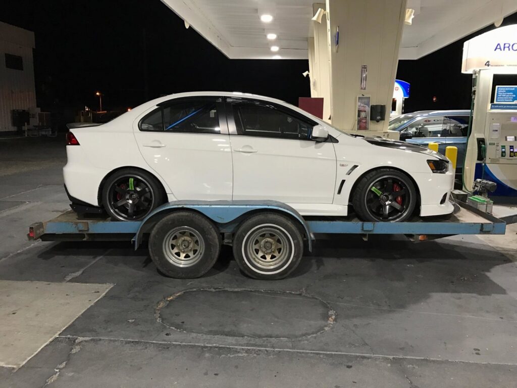 A white sports car on a car trailer at a gas station, transported by Spokane Towing Services in Spokane, WA.