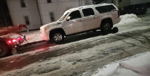 A white SUV being towed on a snowy street by Buffalo Towing Services in Buffalo, NY, with its rear wheels on dollies.