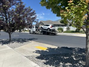 A white SUV being transported on a flatbed tow truck by 4 Wheel Towing on a residential street in South Salt Lake, UT.