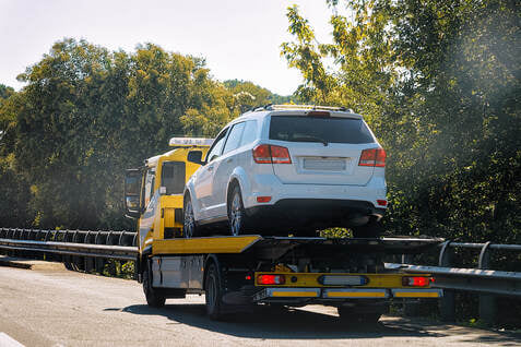 A white SUV being transported on a yellow flatbed tow truck by DunRite Towing Jonesboro in Jonesboro, AR.
