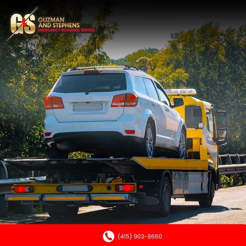A white SUV being transported on a yellow flatbed tow truck by Guzman Towing Services in Oakland, CA.